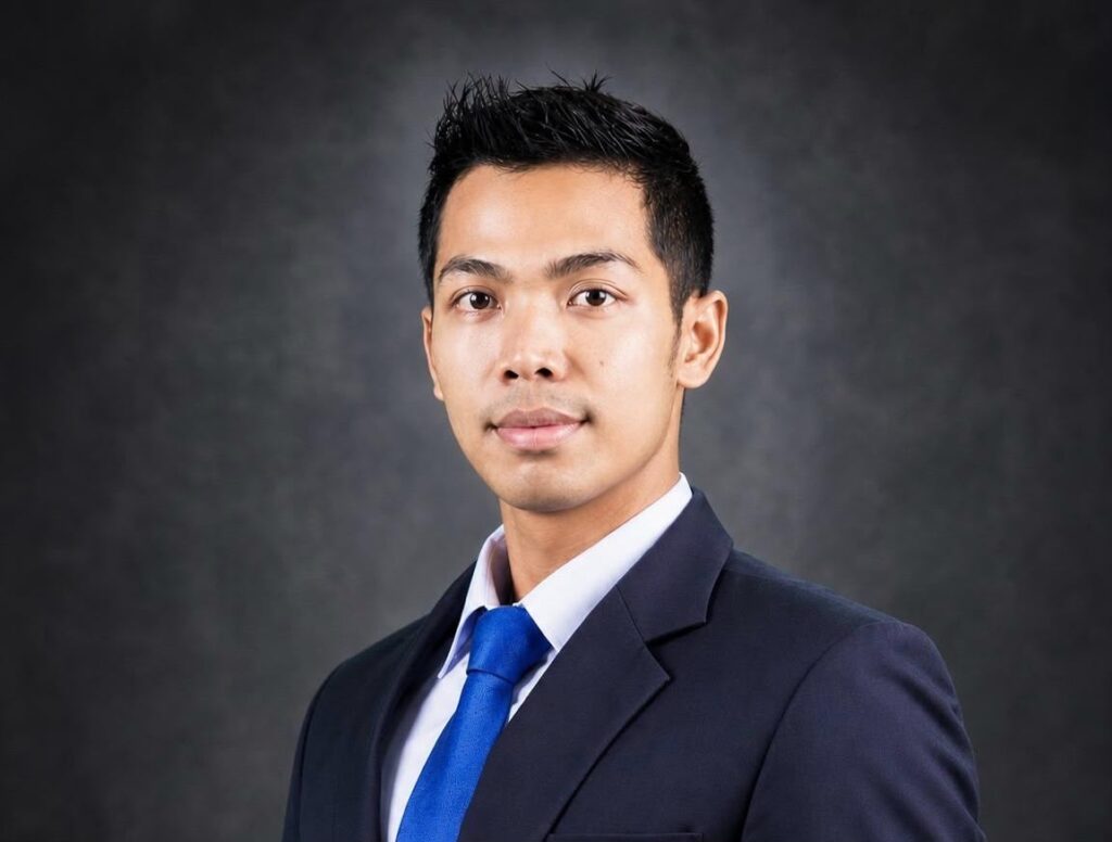 Whatsapp image 20260617 at 20 59 23 catrawarta Professional head and shoulders portrait of a young man in a navy suit and blue tie against a dark gradient background